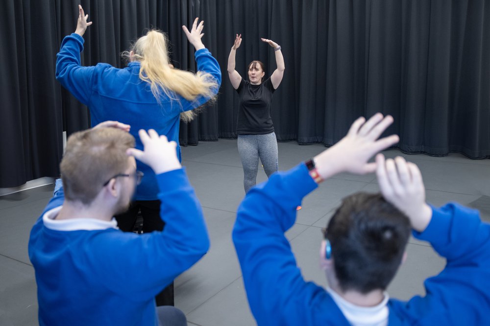 primary school children follow a teacher at the front raising their arms above their heads
