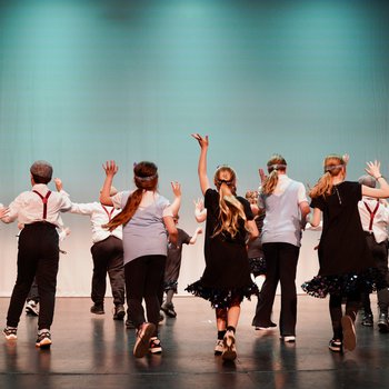Dancers in black, silver and white clothes, standing on a stage facing the back
