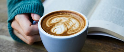 a cup of coffee with latte art next to an open book