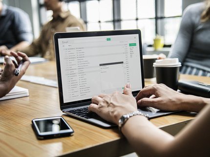 Hands typing on a computer keyboard with a screen on a table
