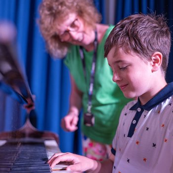 a young boy playing the piano and his female teacher standing to the side of him