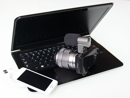 A laptop partly open with a camera and mobile phone resting on the keyboard