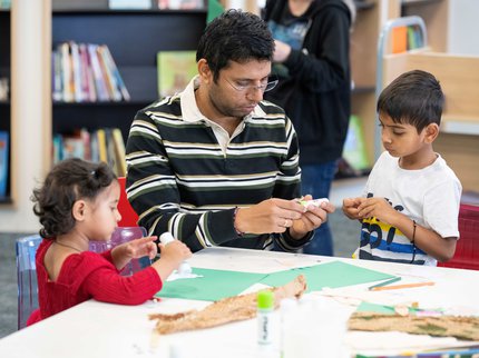 A father and children doing crafts in a library