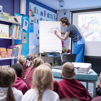 an author writes on a white board in front of a group of sitting children