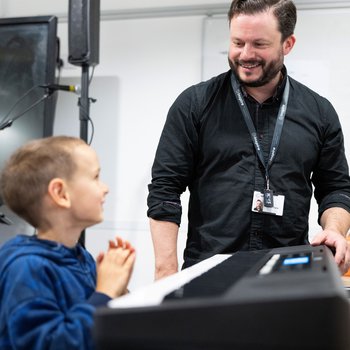 A boy playing the piano and smiling at the musician