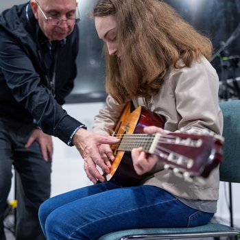 A girl with curly hair being taught how to play the guitar by a musician